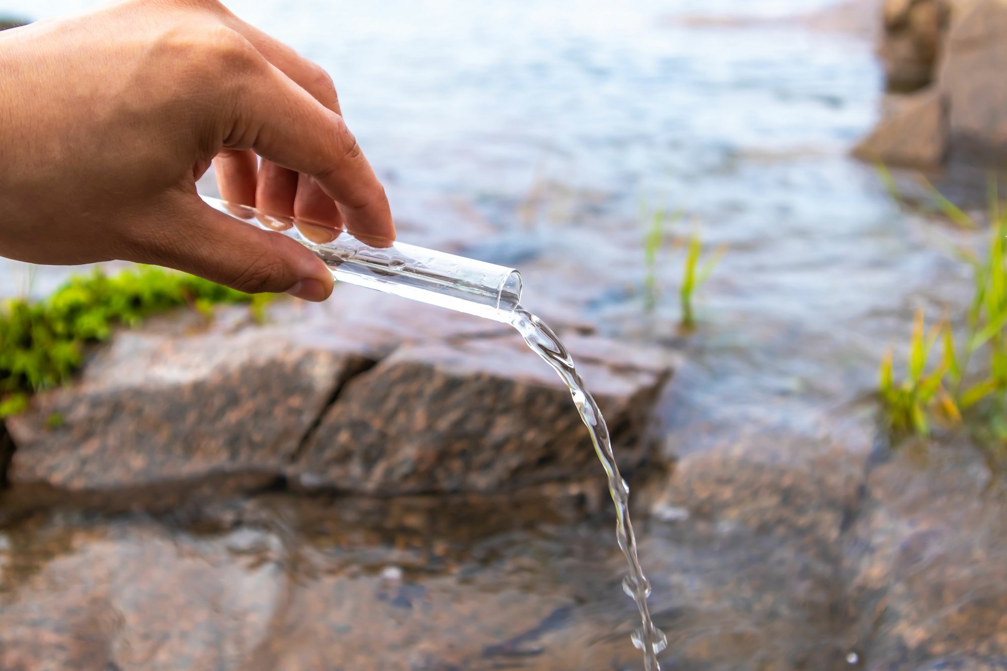 Hand holding a test tube and pouring water out of it in nature. Water purity analysis and environment concept.
